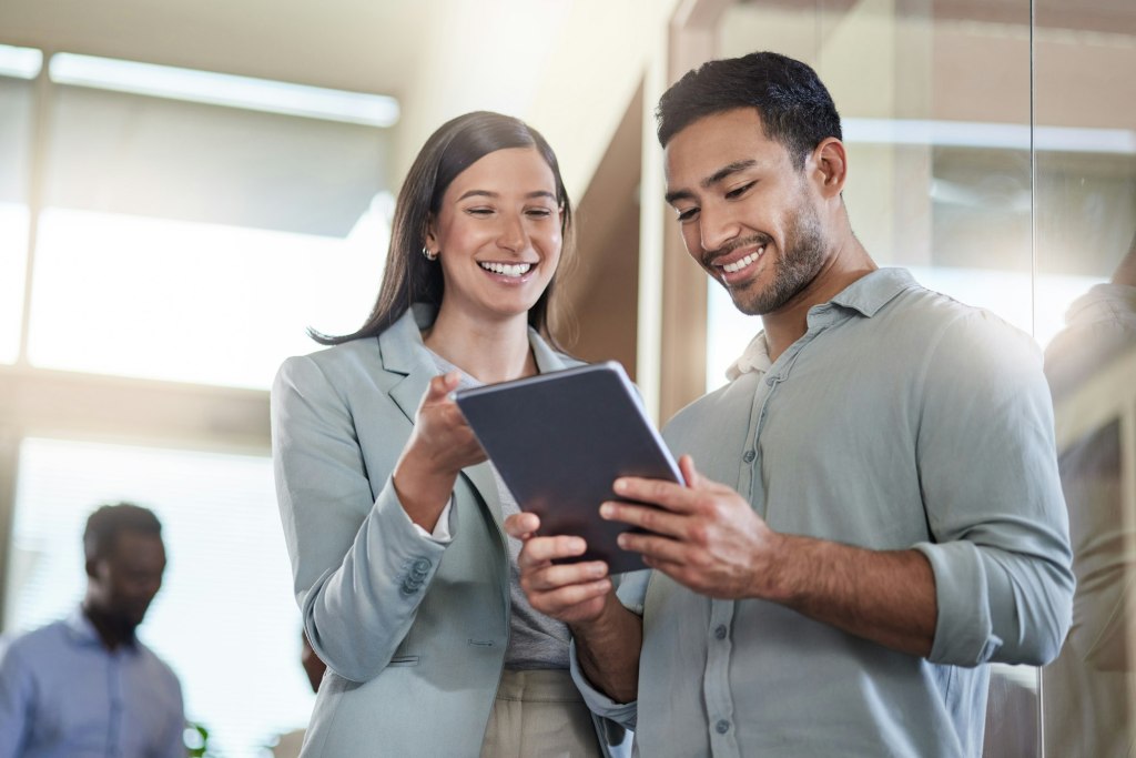 Two coworkers smiling while reviewing something on a tablet